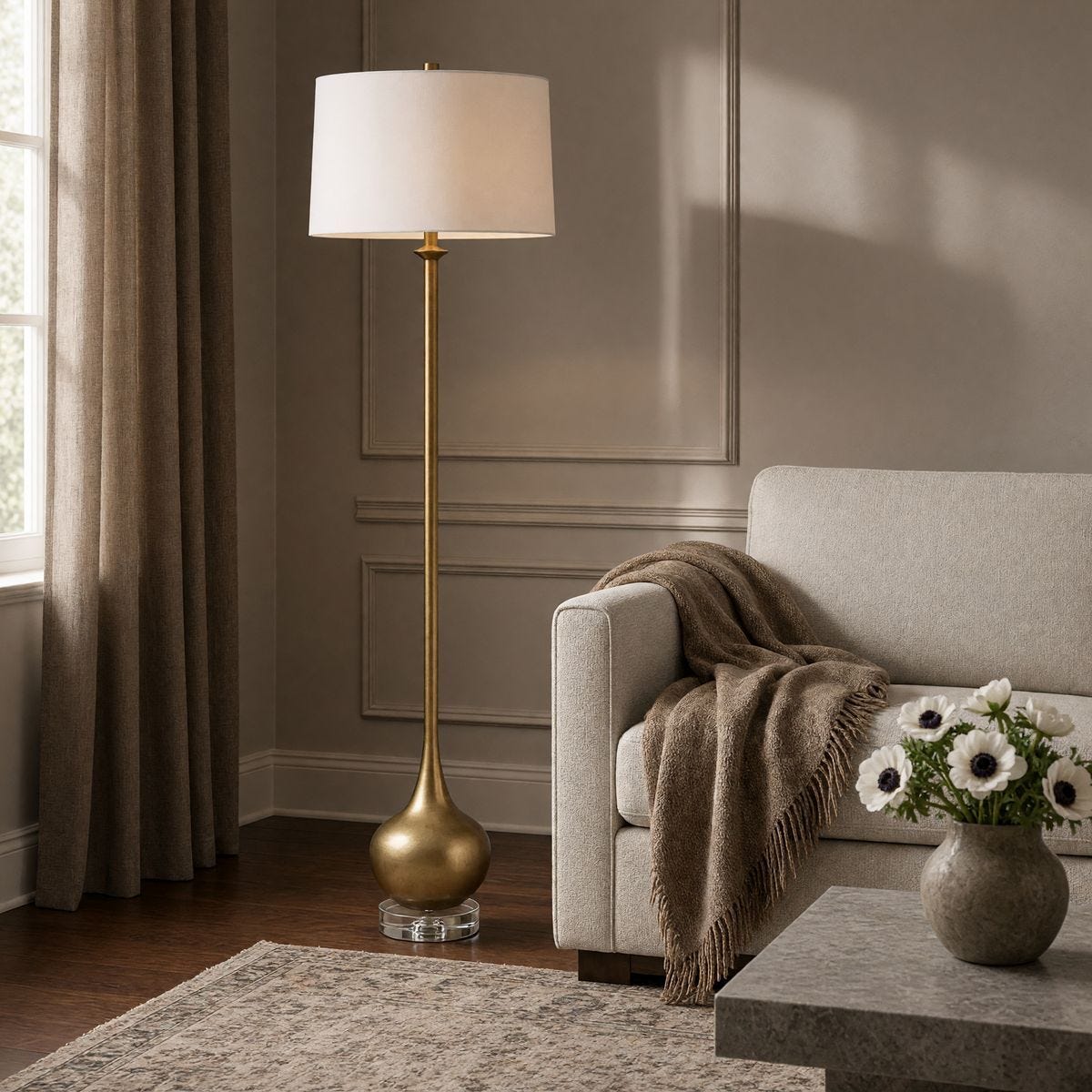 Uttermost Good As Gold brass floor lamp beside a tailored neutral chair, flowers, and a softly layered throw